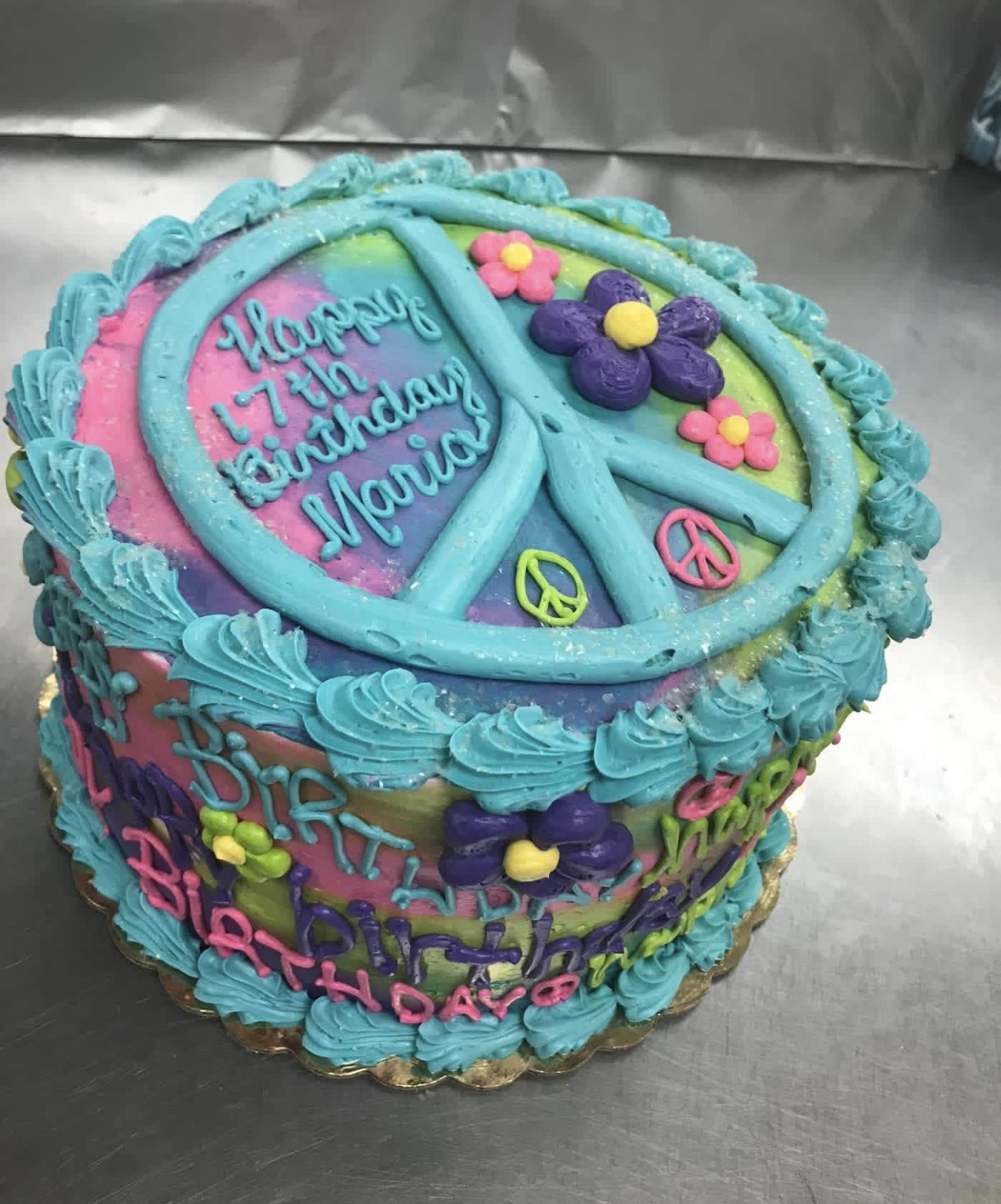 Tie-dye peace sign 17th birthday cake with teal buttercream shells and flowers